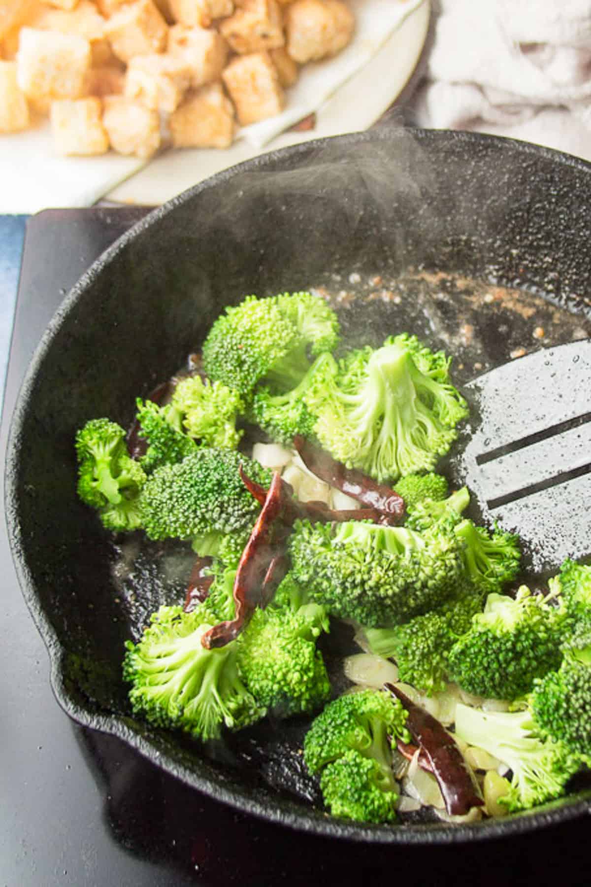 Broccoli and aromatics stir frying in a skillet.