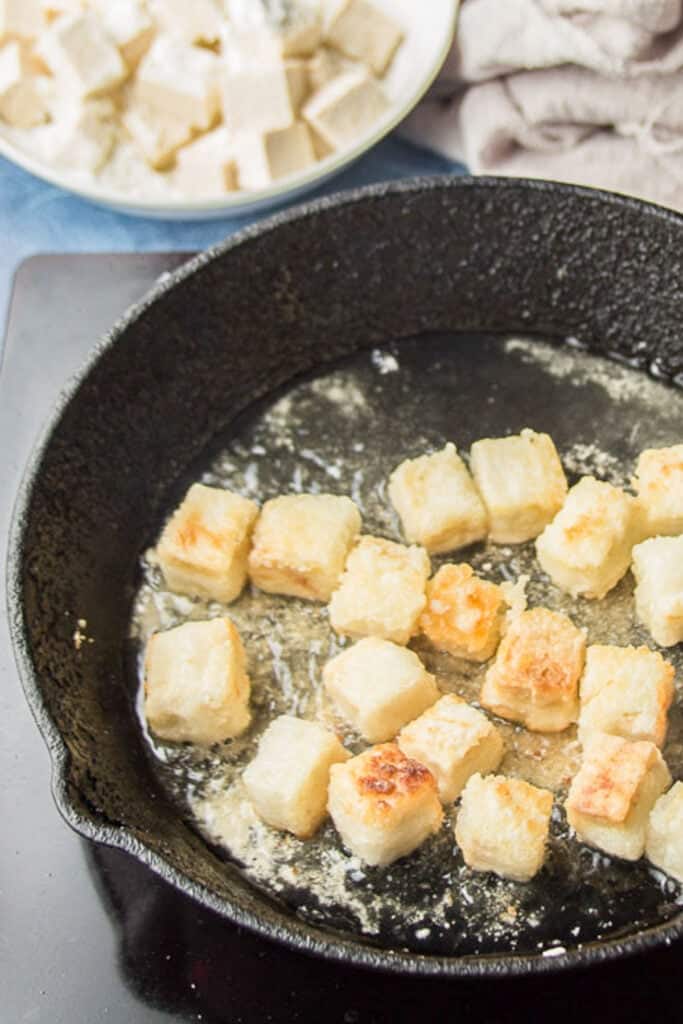Cornstarch-coated tofu cubes frying in oil.