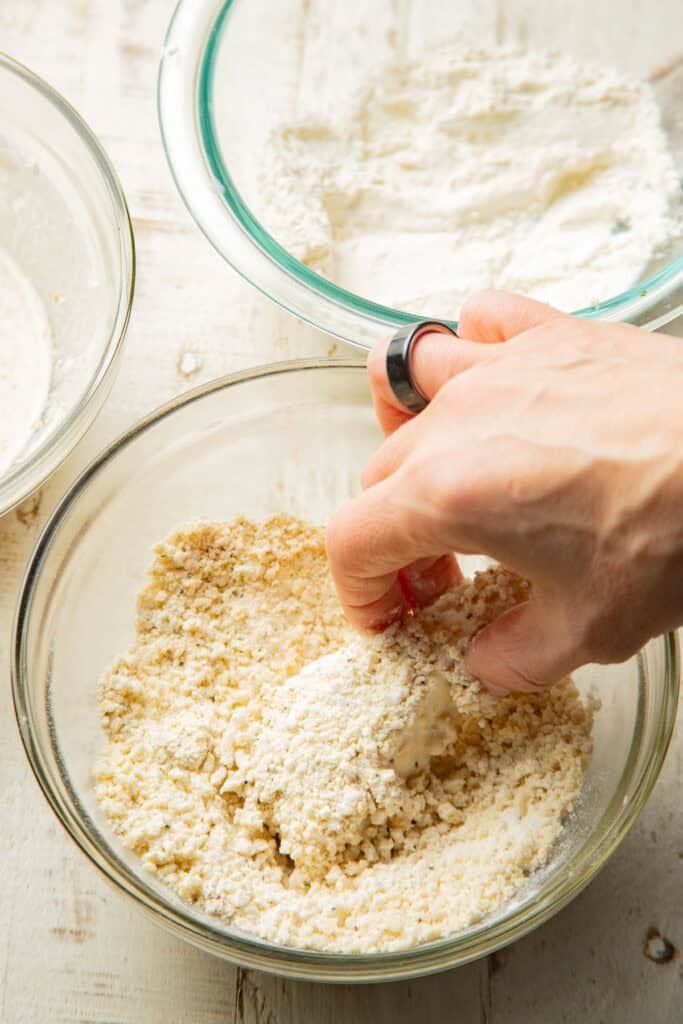 Hand dipping a tofu triangle in breading.
