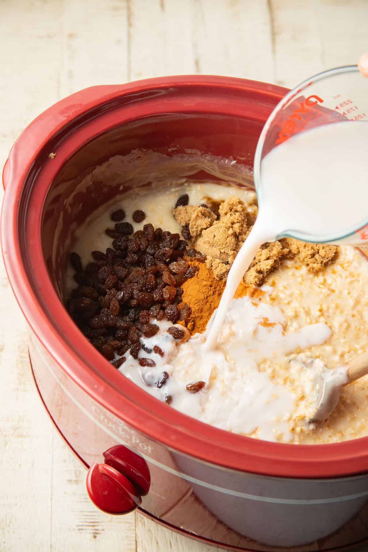 Non-dairy milk being poured over ingredients for cinnamon raisin oatmeal in a slow cooker.