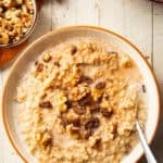 White wooden surface set with a bowl of Slow Cooker Oatmeal, slow cooker, and bowl of walnuts.