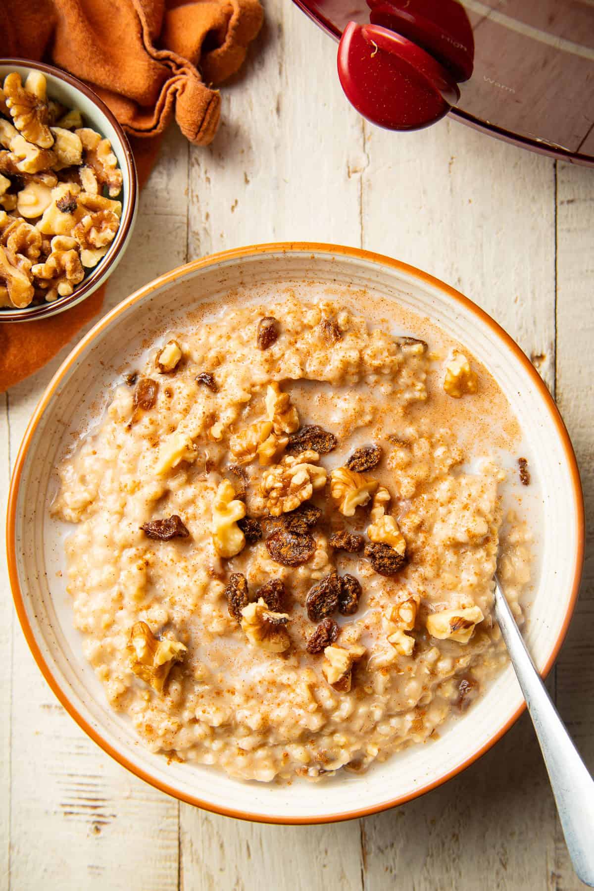 White wooden surface set with a bowl of Slow Cooker Oatmeal, slow cooker, and bowl of walnuts.