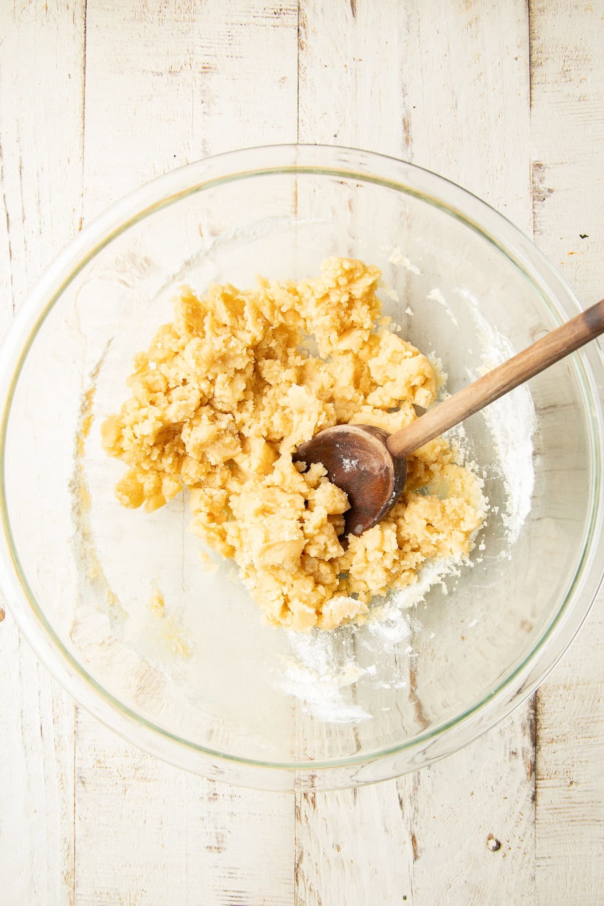 Shortbread press in crust dough in a mixing bowl with wooden spoon.
