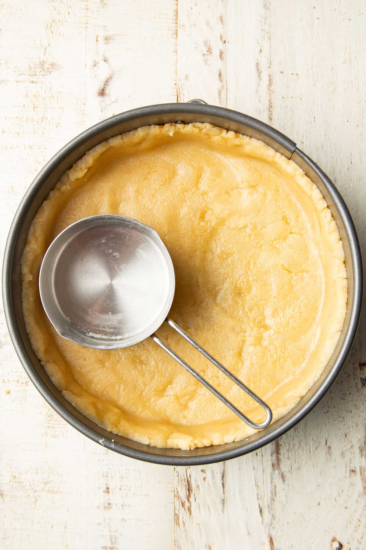 Unbaked press in shortbread crust in a springform pan with dry measuring cup inside.