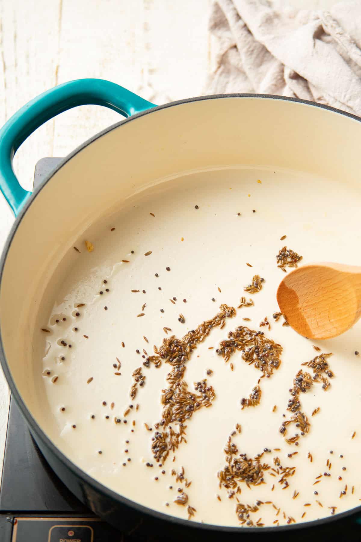 Cumin and mustard seeds cooking in oil in a pot.
