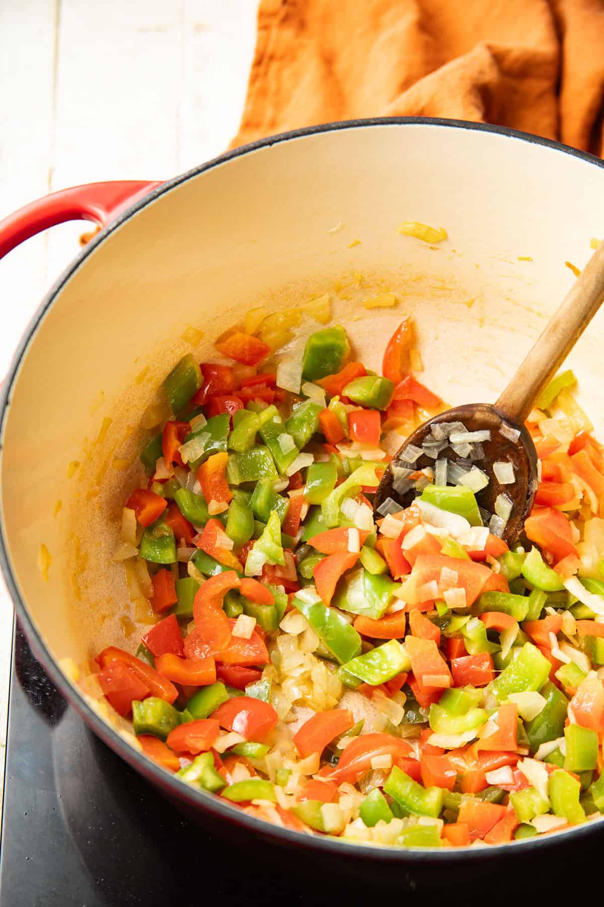 Diced peppers and onions cooking in a pot with wooden spoon.