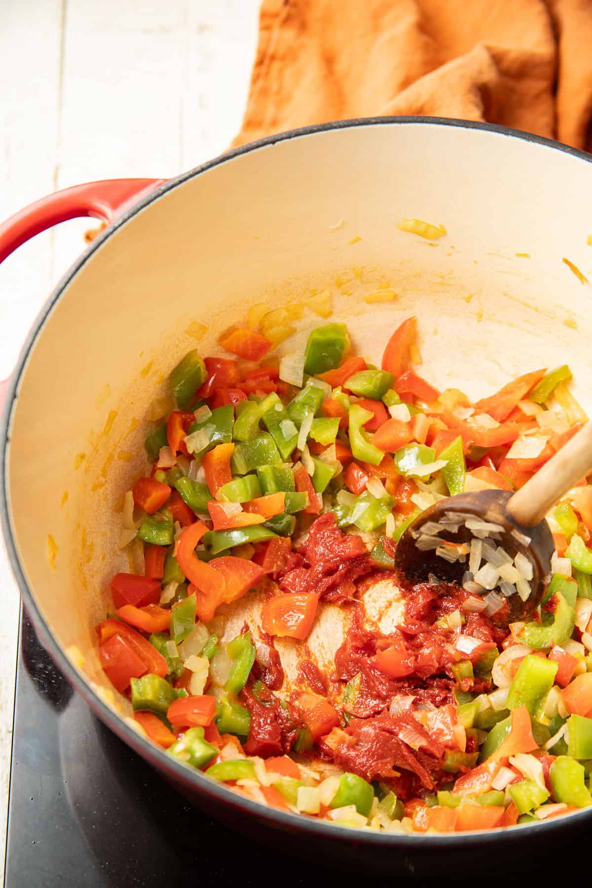 Tomato paste cooking in a pot with diced peppers and onions.