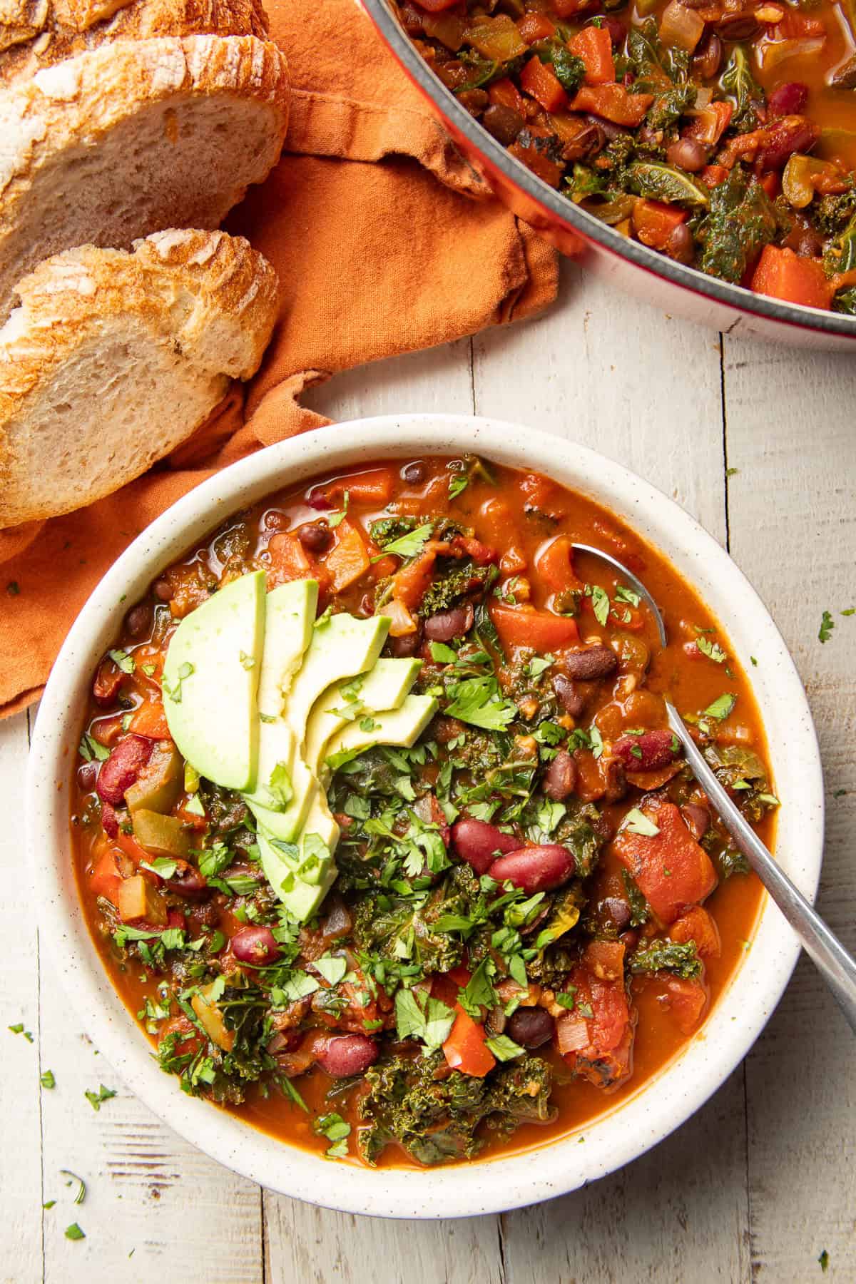 White wooden surface set with bowl and pot of Kale Chili.