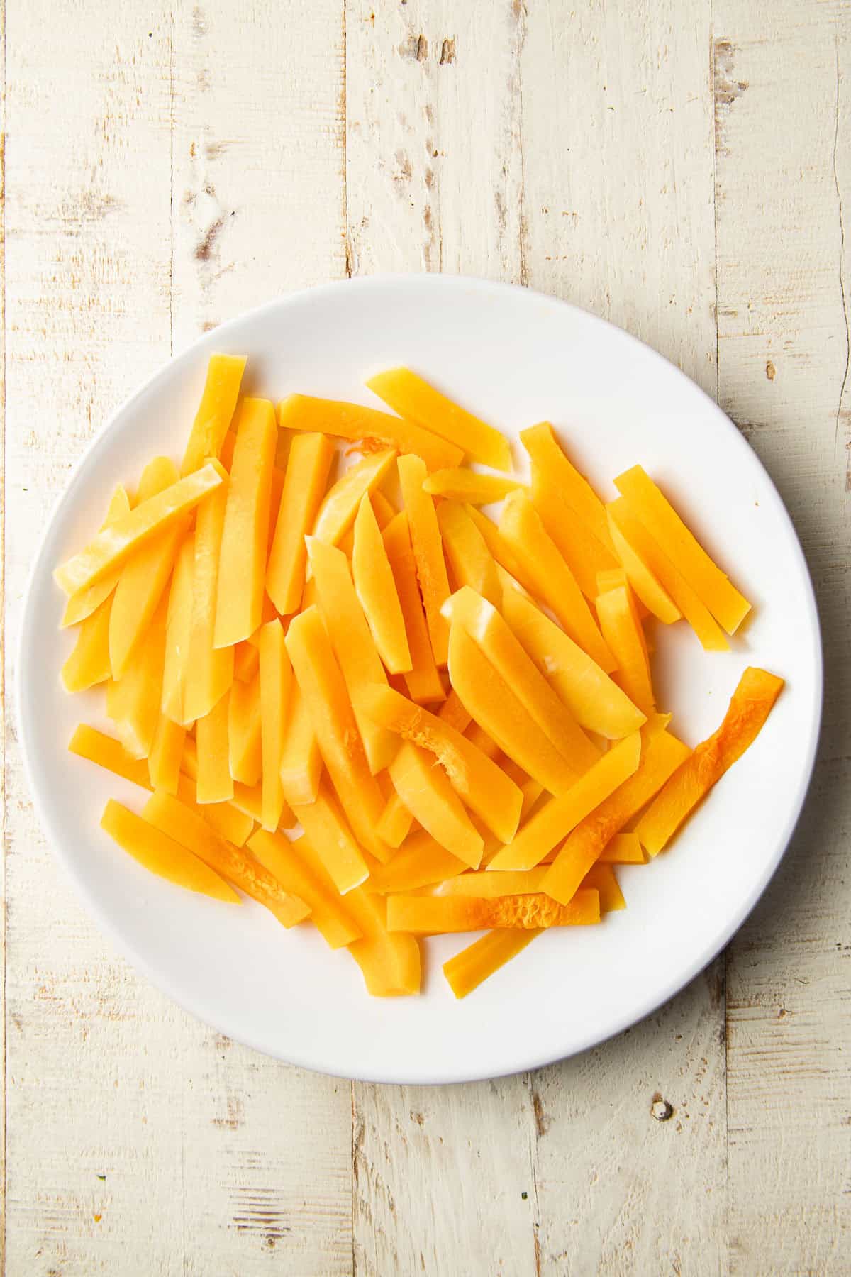 Partially cooked butternut squash batons on a plate.