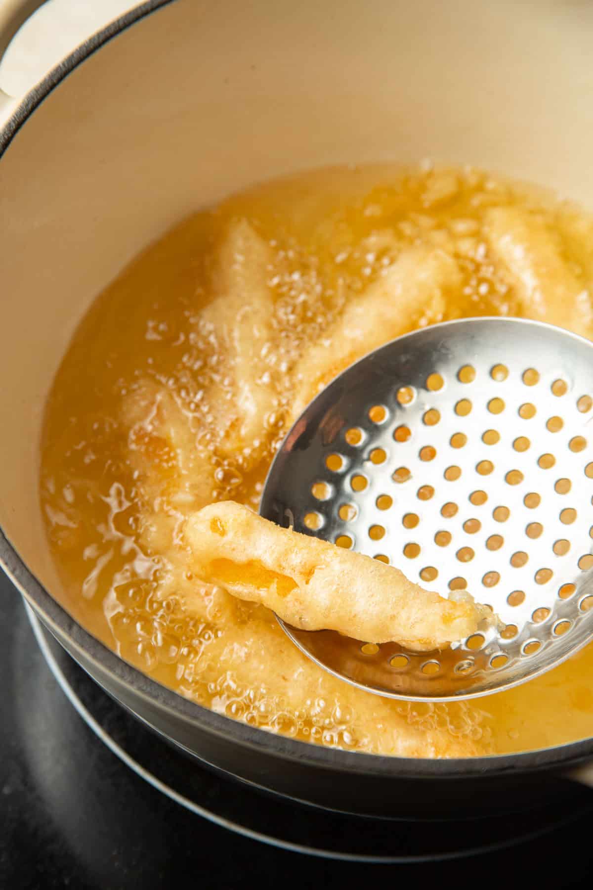 Slotted spoon removing a tempura fried butternut squash baton from frying oil.