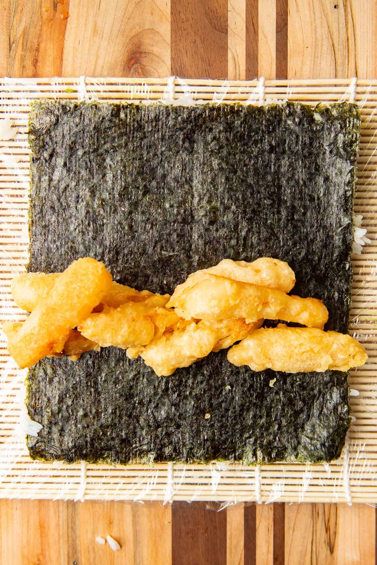 Tempura fried squash batons on a sheet of nori with rice on the bottom.