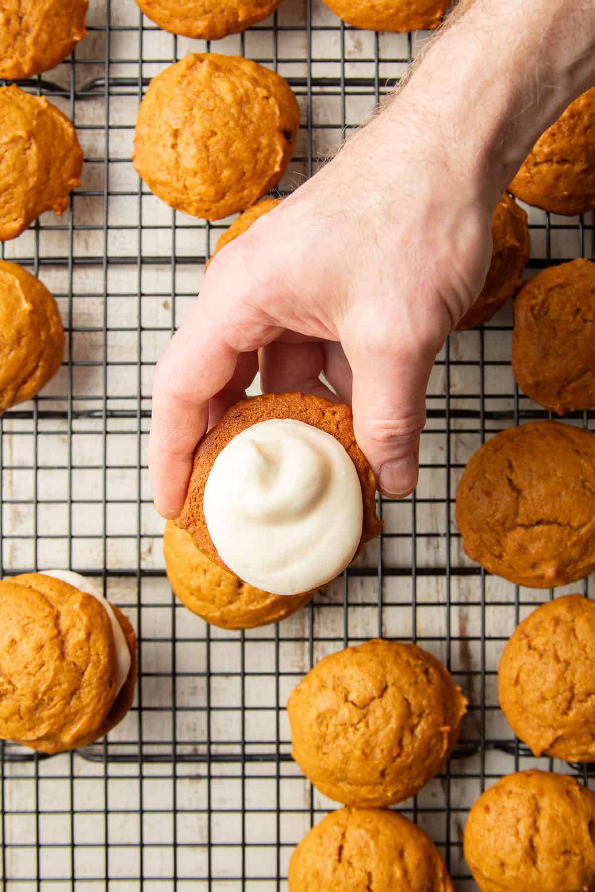Hand holding half a Vegan Pumpkin Whoopie Pie with filling over a cooling rack.