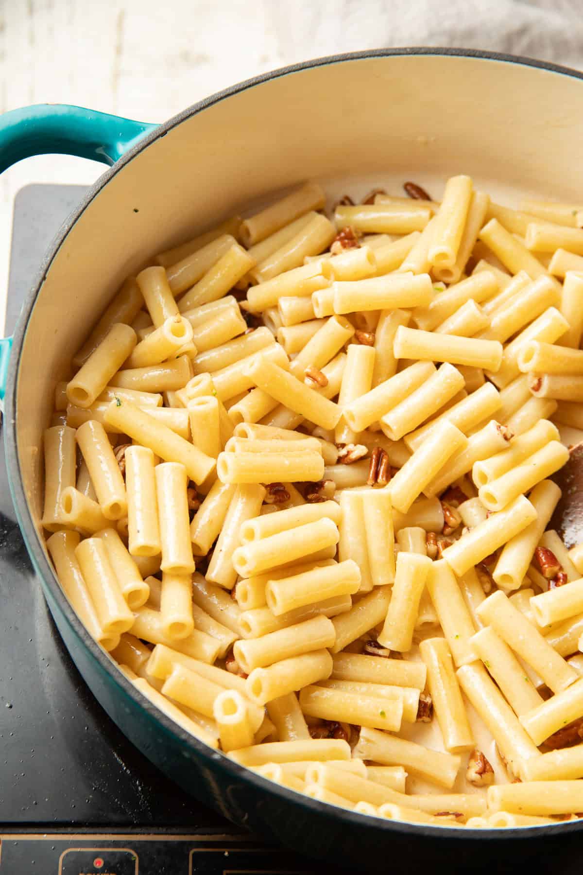 Pasta and chopped pecans in a pot with vegan brown butter sauce.