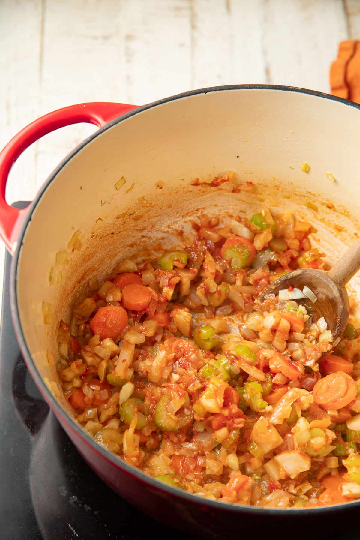 Carrots, celery, and onion cooking in a pot with tomato paste.