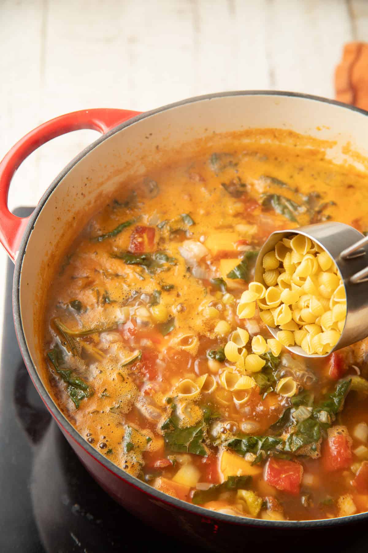 Mini pasta shells being added to a simmering pot of Fall Minestrone.