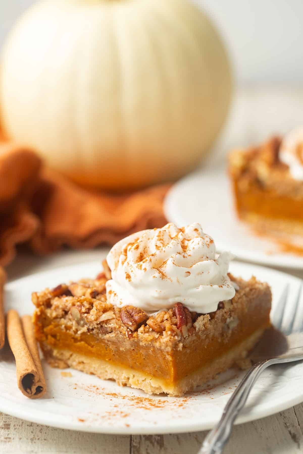 Pumpkin pie bar on a plate with a white pumpkin in the background.