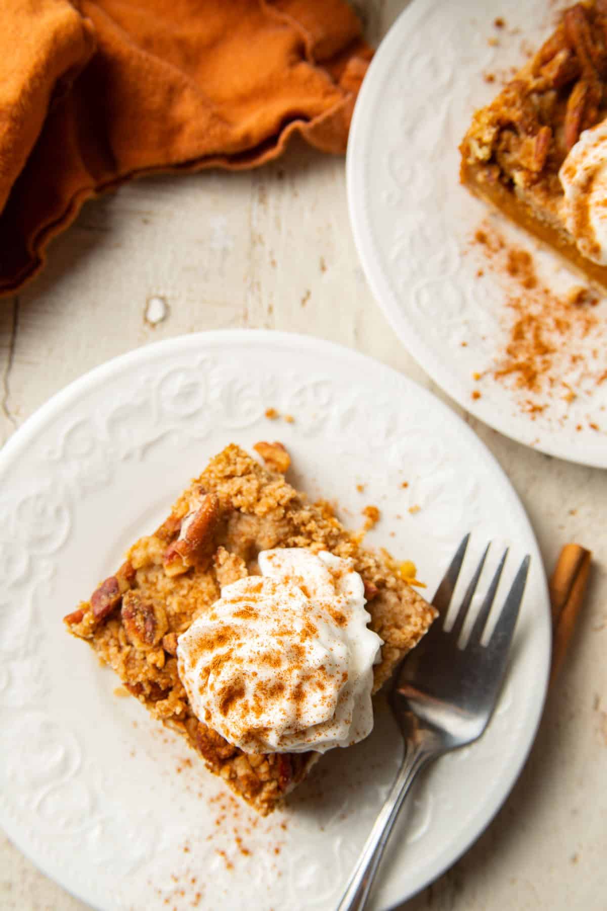 White wooden surface set with two Pumpkin Pie Bars on plates.