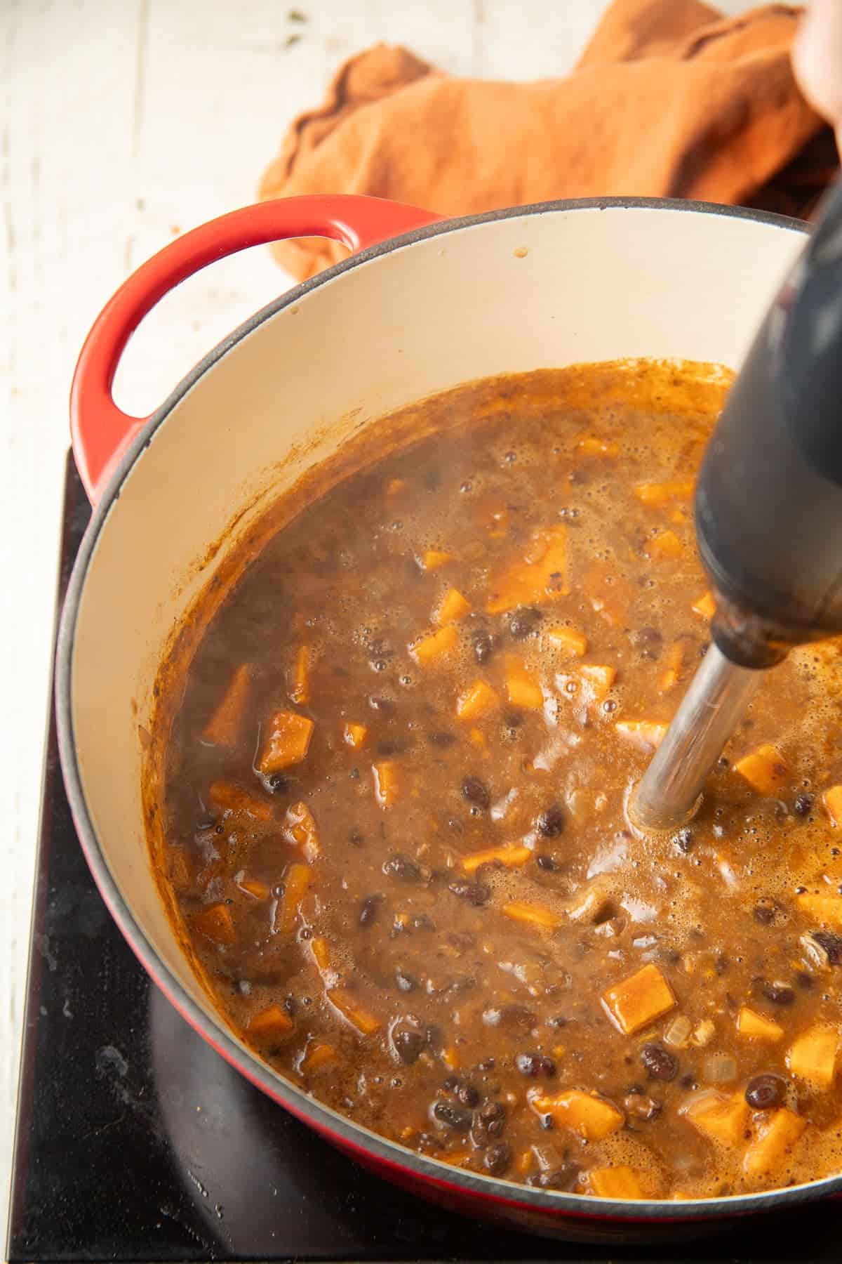 Immersion blender blending Sweet Potato Black Bean Soup in a pot.